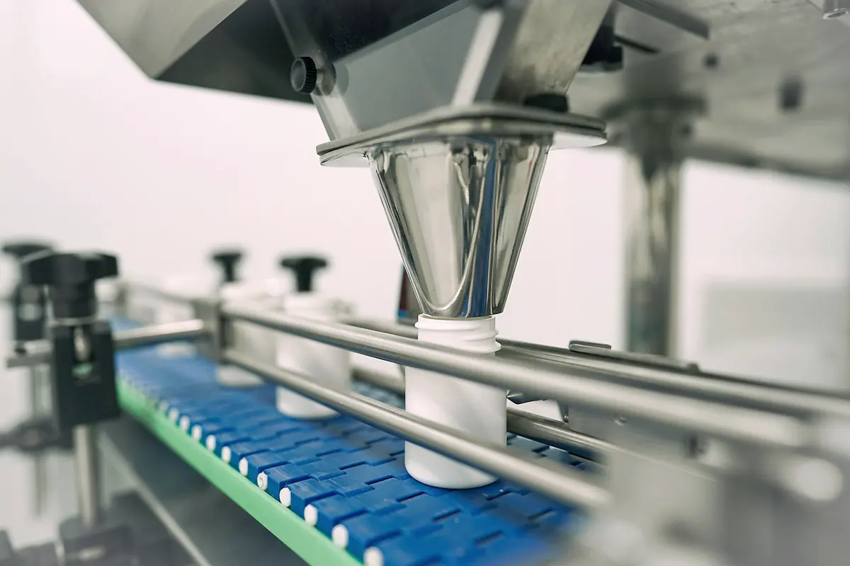 A stainless filling head dispensing into a bottle on a conveyor