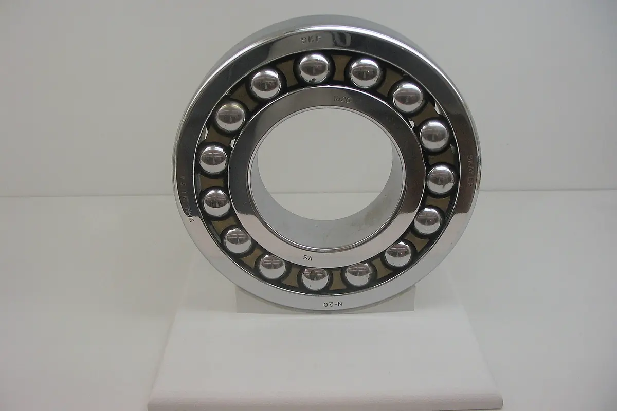 A polished self-aligning ball bearing standing on a plain white plinth