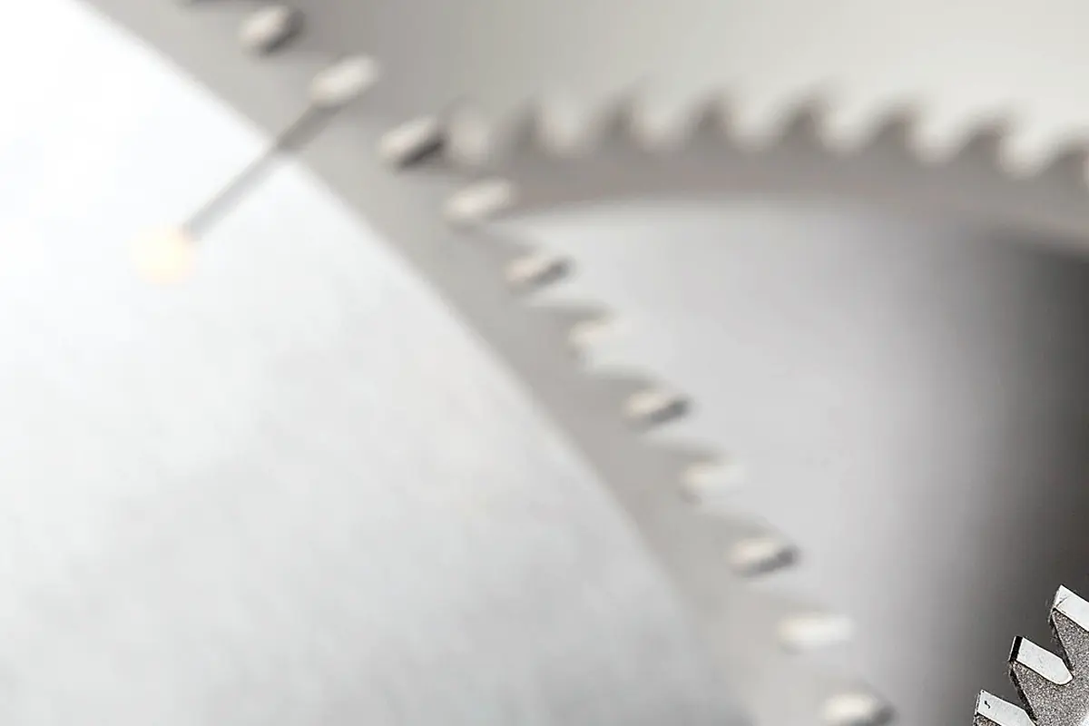 Macro of the carbide-tipped teeth of a circular saw blade, more blades stacked behind
