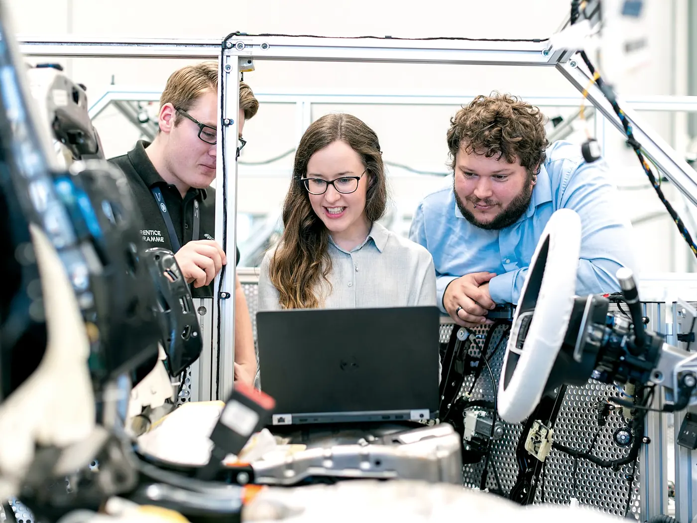 Three engineers leaning over a laptop set on a test frame in a bright assembly bay