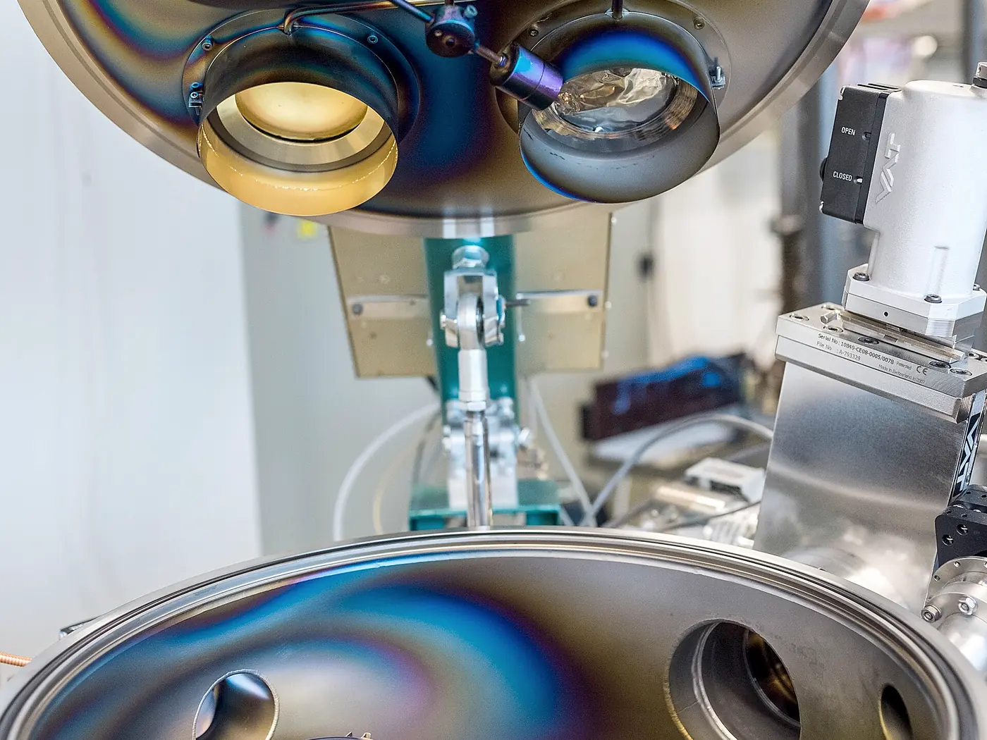 The open lid and base of a vacuum deposition chamber, source heads above a substrate holder